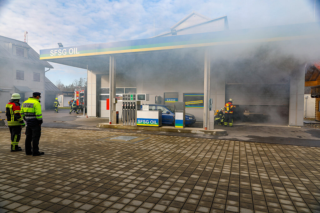 A burning, smoking gas station where firefighters are extinguishing