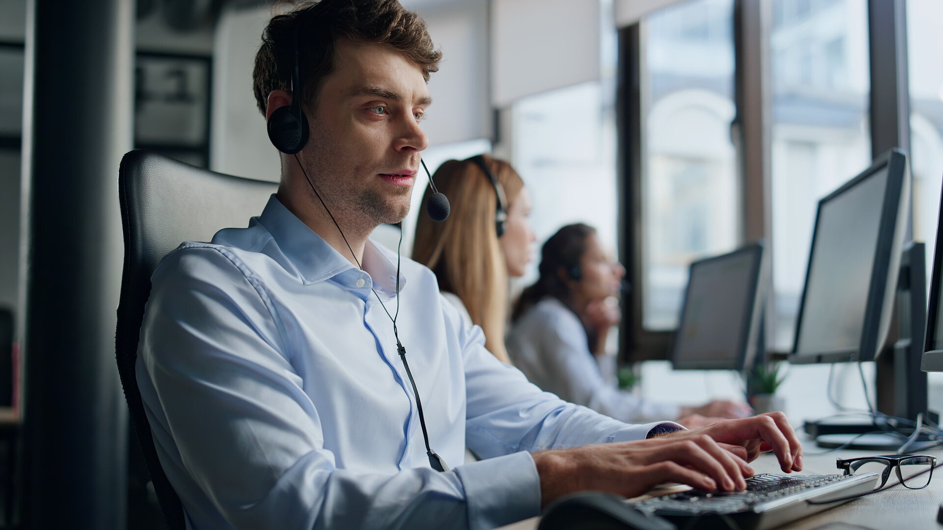 Menschen in einem Callcenter an Pcs, ein Headset tragend und telefonierend