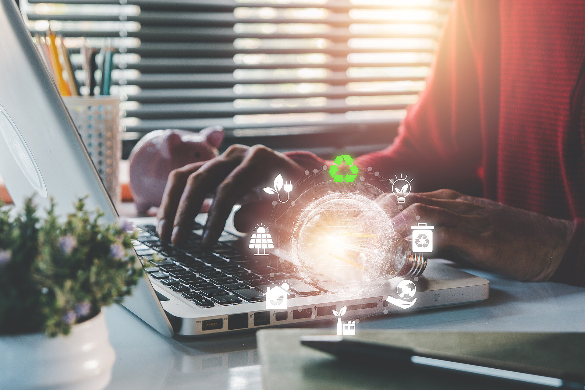 Eine Person arbeitet an einem Laptop an einem Schreibtisch. Dort stehen eine Pflanze und ein Stift. Dazu eine Visualisierung, die einer Glühlampe ähnelt