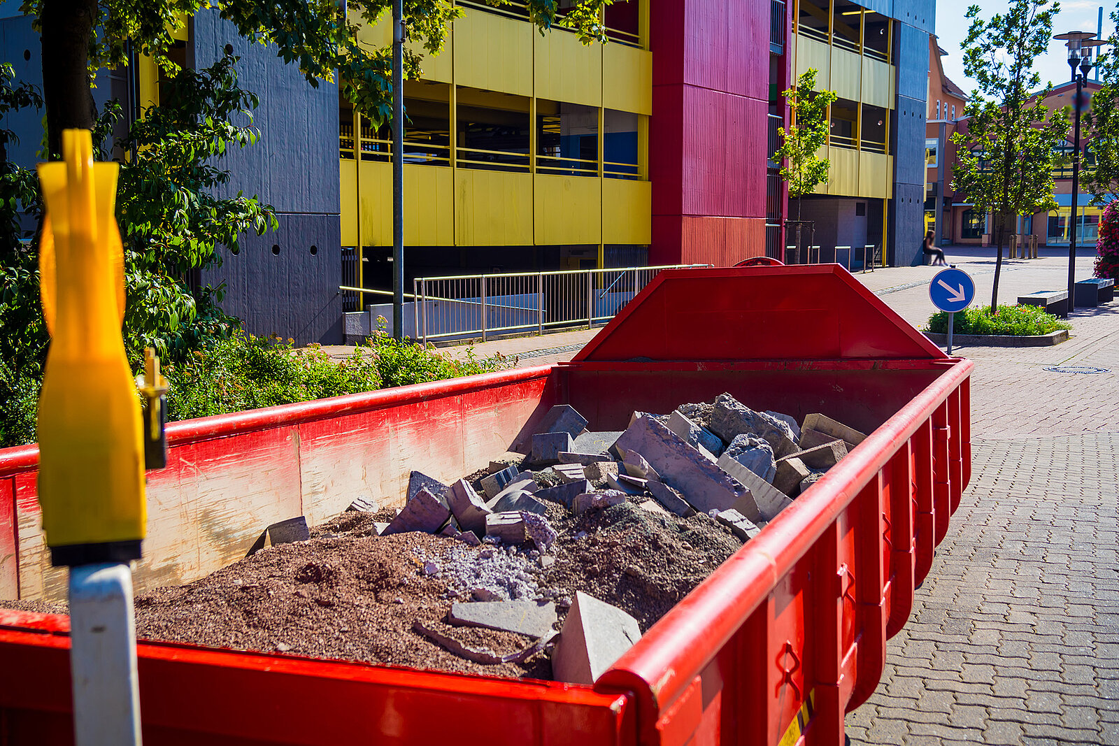 A metal tub containing construction waste. A building in the background
