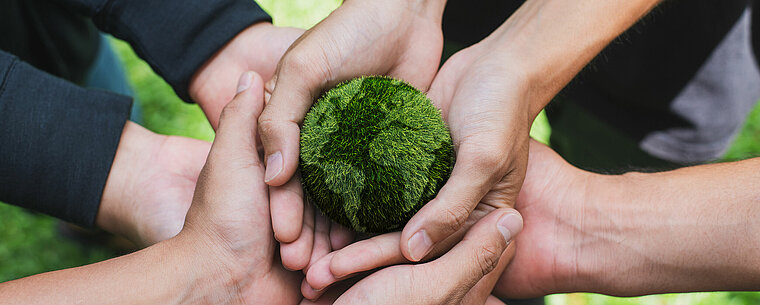 Mehrere Hände halten eine kleine Miniatur-Erde in grün fest
