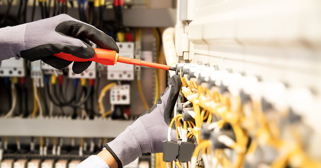 Eine Person mit Handschuhen tätigt mithilfe eines Schraubenziehers eine Elektroinstallation