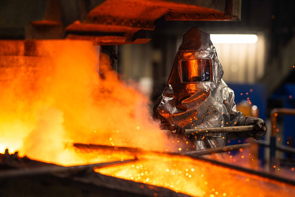 Arbeiter, der mit Schutzmontur Stahl in Feuer bearbeitet