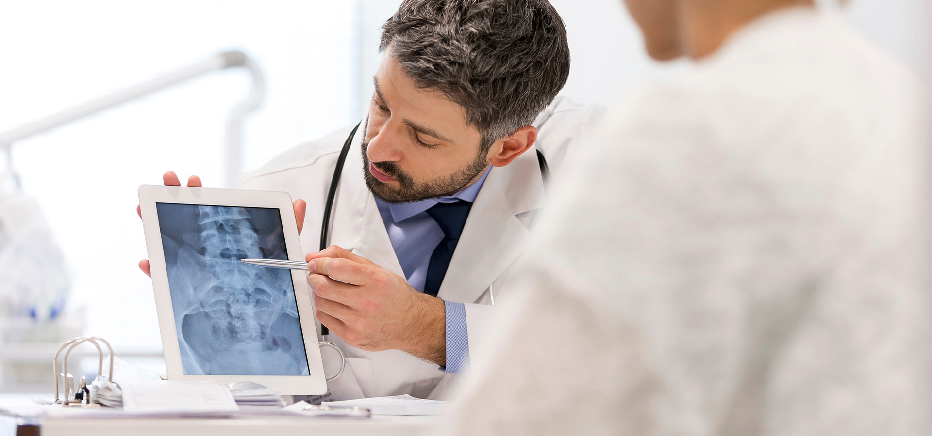 Ein Doktor zeigt einem Patienten ein Röntgenbild auf einem Tablet.