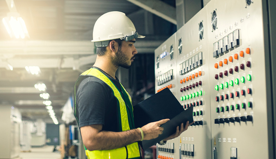 Ein Mann in Arbeitskleidung mit einem Block im Arm, vor ihm ist ein Stromkasten