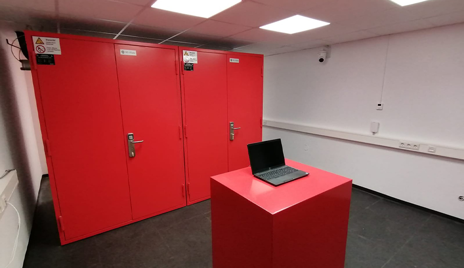 2 DC IT Container in rot, im Vordergrund ein rotes Podest, auf dem ein Laptop steht